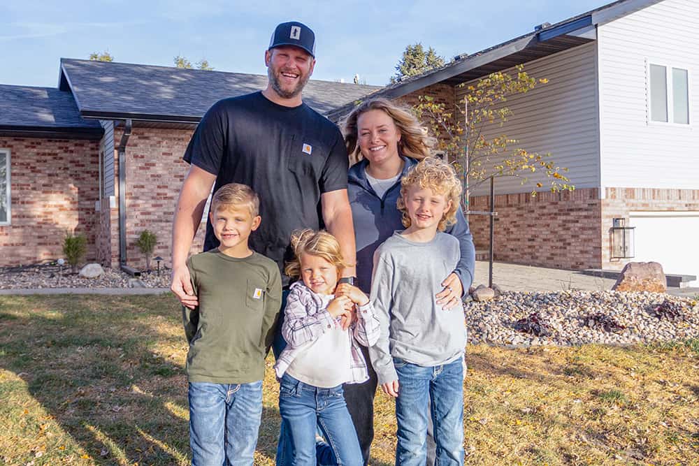 Farm family with children stands before farmhouse